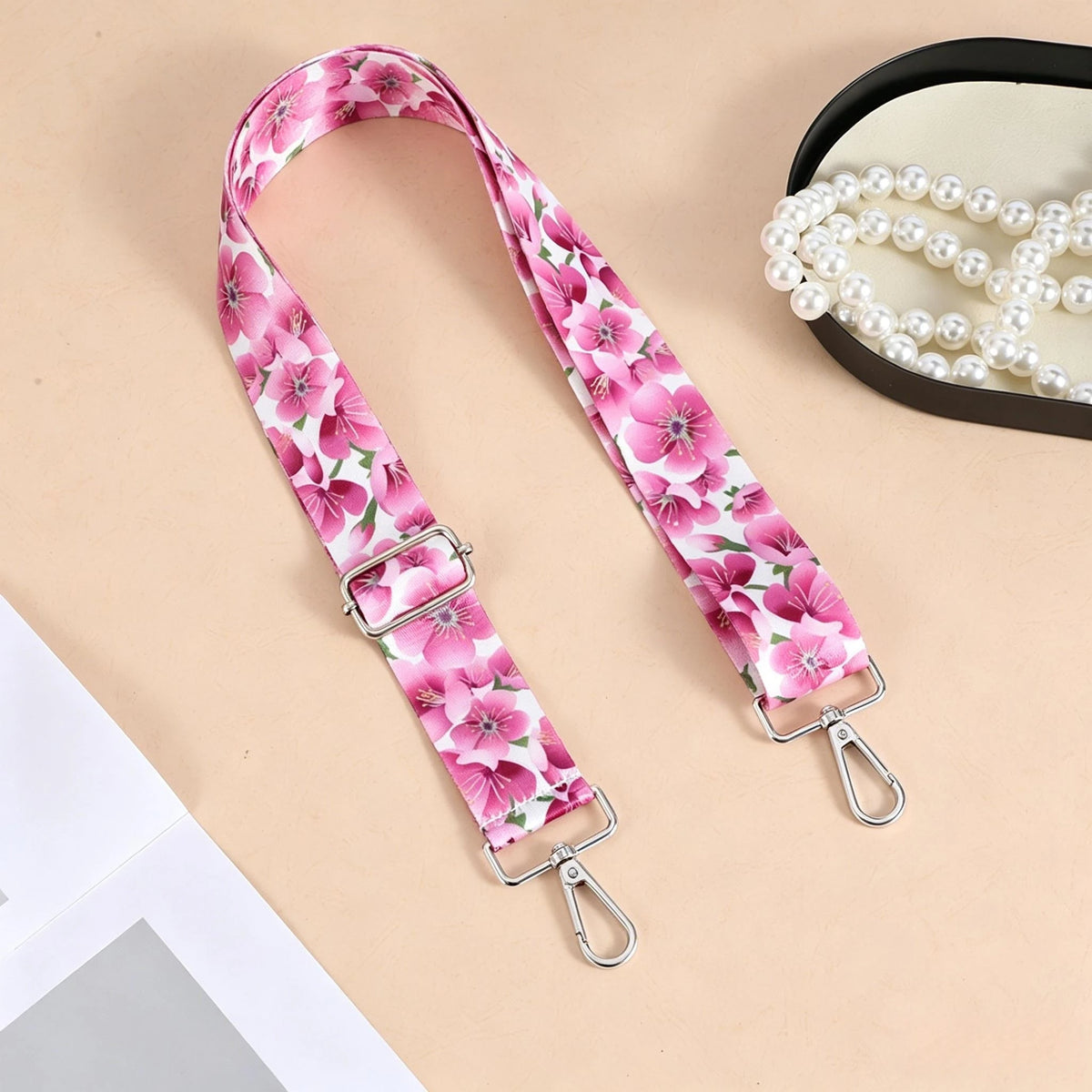 Pink floral patterned nylon crossbody bag strap with a silver metal buckle displayed on a beige background.