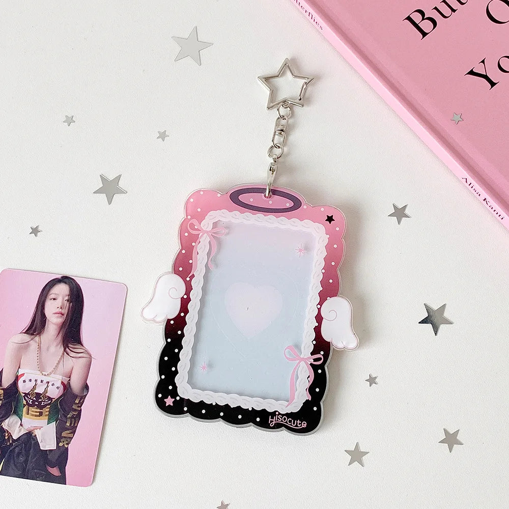 A pink and black angel wings photocard holder with a clear display case and a silver charm