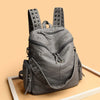 Sac à dos en cuir souple gris rivetée de luxe posé sur une surface en bois clair.