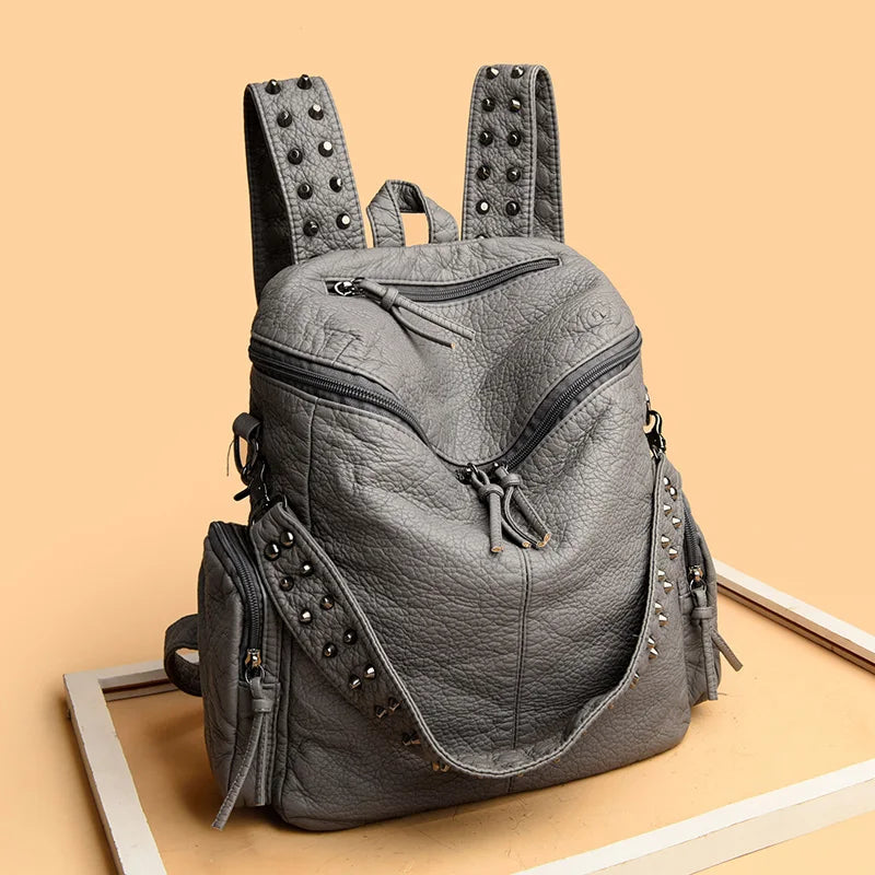 Sac à dos en cuir souple gris rivetée de luxe posé sur une surface en bois clair.
