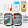 A compact survival and first aid kit displayed with various components including a pouch, bandages, and a yellow packet.