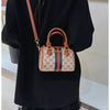 A brown leather tote diaper bag with a green and red striped fabric detail is shown against a black top.