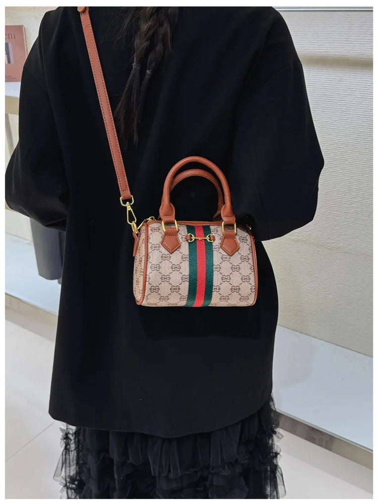 A brown leather tote diaper bag with a green and red striped fabric detail is shown against a black top.