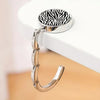 A silver metal round bag hanger with a black and white zebra pattern is displayed on a white surface.