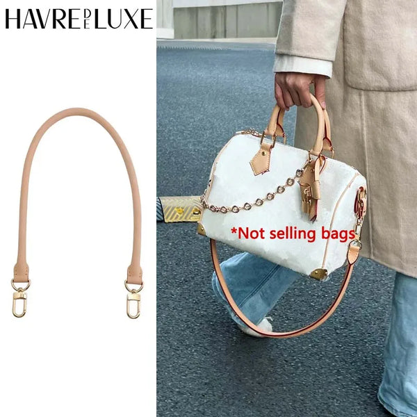 A beige leather shoulder strap is shown attached to a white handbag being carried by a person.