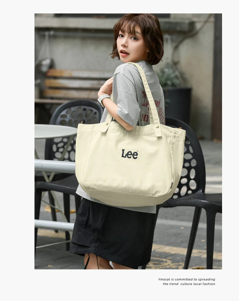A woman models a cream-colored Korean style Oxford cloth tote bag in an outdoor setting.
