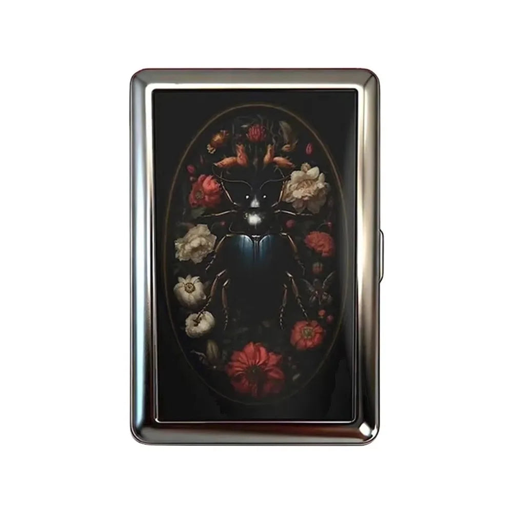 A vintage snap metal card holder with a dark background featuring an ornate floral design.