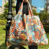 A large, colorful fabric shopping tote bag featuring an intricate floral pattern is held by a person outdoors.