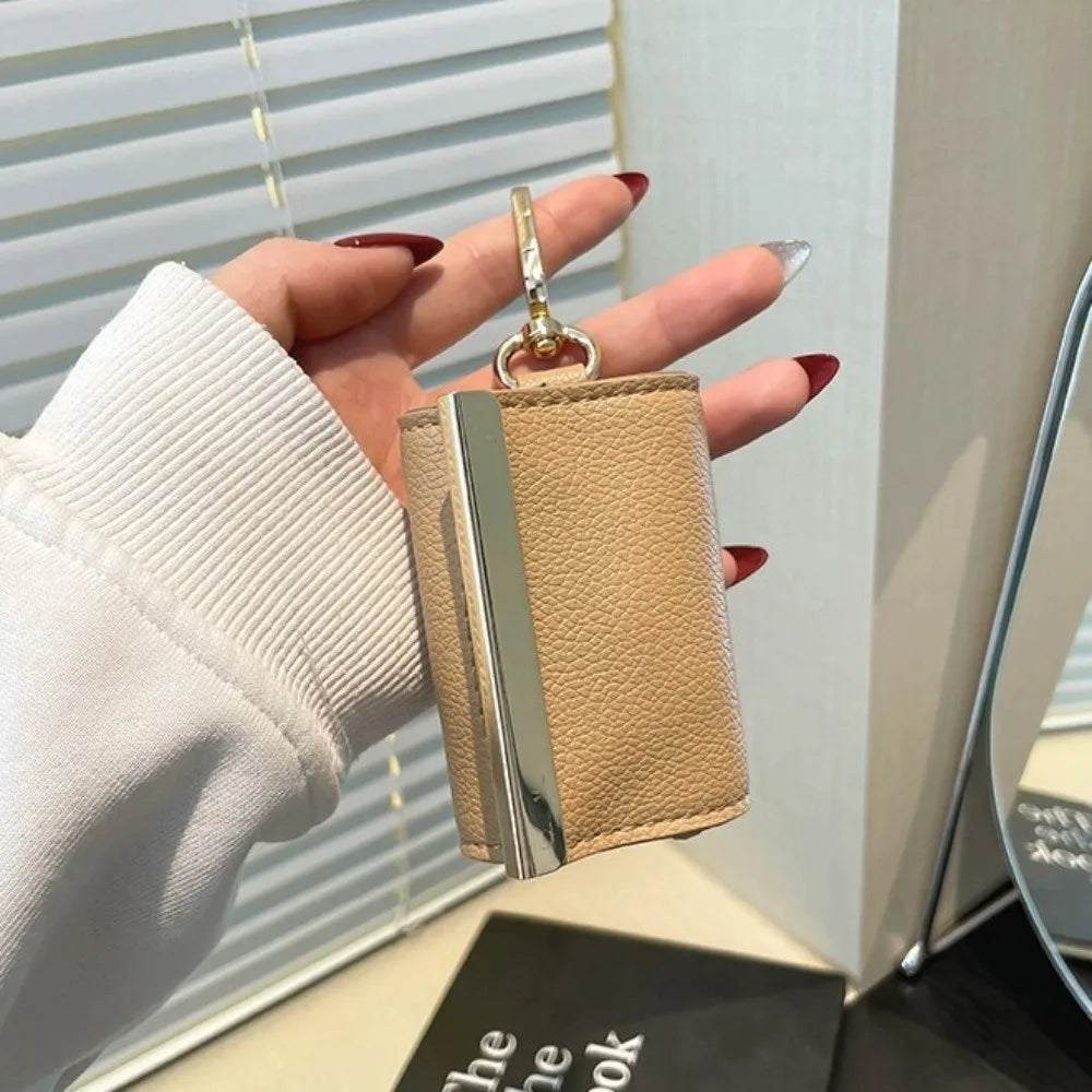 A hand holds a beige nylon mini keychain tote bag with a silver clasp against a light background.
