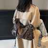 A woman is shown from the back wearing a beige trench coat and carrying a brown leather commuter shoulder bag.