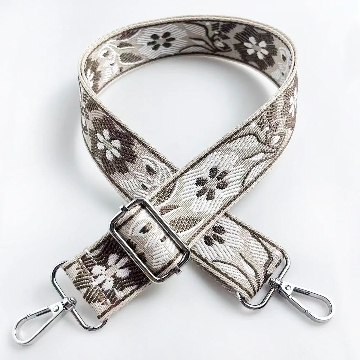 A beige and black floral patterned fabric strap with a silver buckle shown against a white background.
