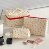 A cream quilted makeup bag with a red trim and a cartoon animal design, shown next to various beauty products.