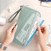 Une main tient un porte-documents organisateur de voyage vert clair pour cartes et documents sur un fond clair.