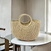 A natural beige handwoven rattan beach bag resting on a white table.