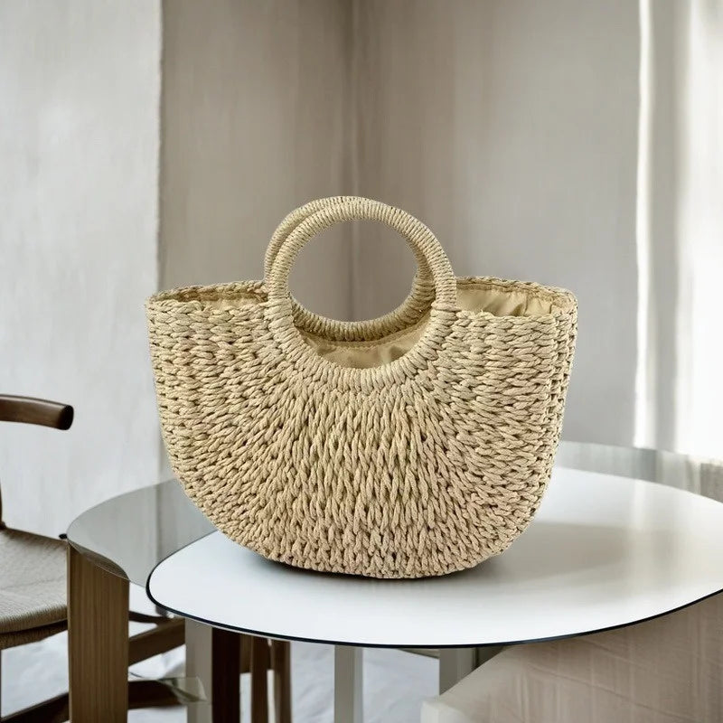 A natural beige handwoven rattan beach bag resting on a white table.