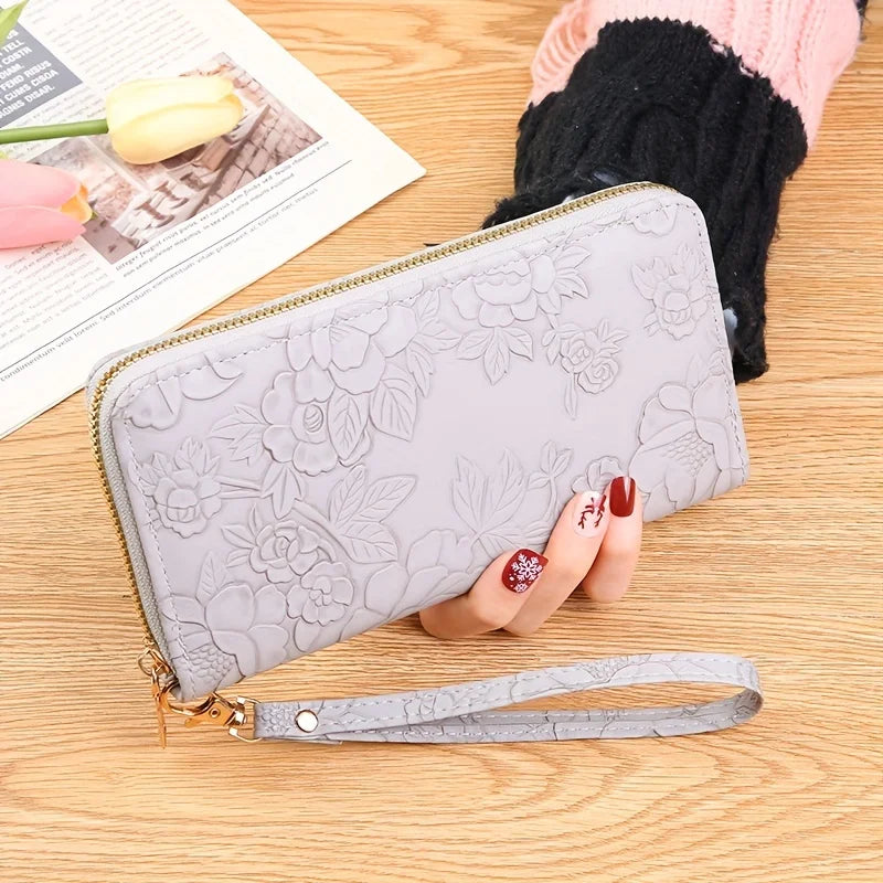 Cartera de tarjeta de cuero PU floral gris claro con cremallera y correa dorada sobre una superficie de madera.
