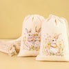 A set of six light beige drawstring gift bags featuring watercolor illustrations of baby rabbits and flowers.