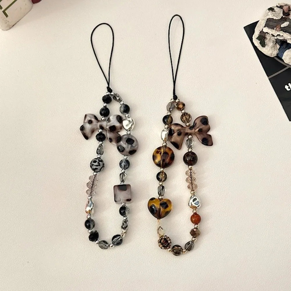 A pair of leopard print bowknot phone lanyards featuring heart and silver beads.