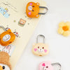 A collection of cute, bear-themed combination padlocks in orange and pink colors resting on a light yellow notebook.