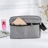 A gray toiletry bag with a zippered compartment holding a light pink cosmetic item and a small glass bottle.