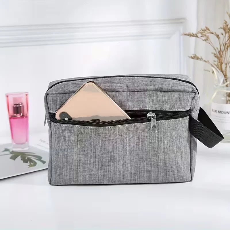 A gray toiletry bag with a zippered compartment holding a light pink cosmetic item and a small glass bottle.