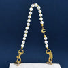 A pearl and gold letter charm necklace displayed on a white quilted bag.