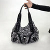 A black leopard print crossbody shoulder bag with multiple compartments being held by a hand.