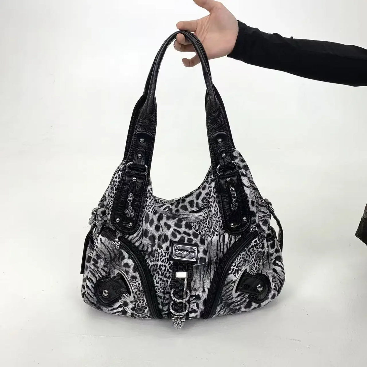 A black leopard print crossbody shoulder bag with multiple compartments being held by a hand.