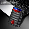 A black carbon fiber slim wallet is shown open on a dark surface next to a laptop keyboard.