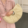 A person holds a cream colored rattan half-moon beach handbag against a pink shirt.
