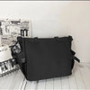 A black nylon crossbody bag is displayed on a white surface next to some printed materials.