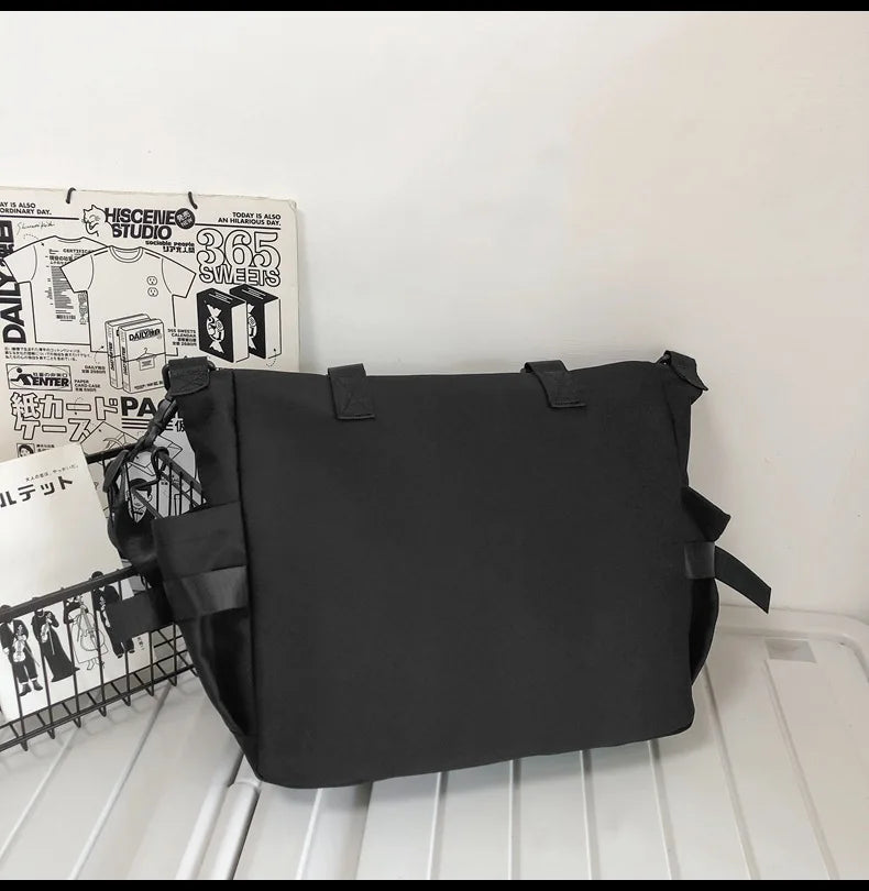 A black nylon crossbody bag is displayed on a white surface next to some printed materials.