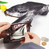 A hand is opening a dark patterned fish-shaped pencil case to reveal money inside.