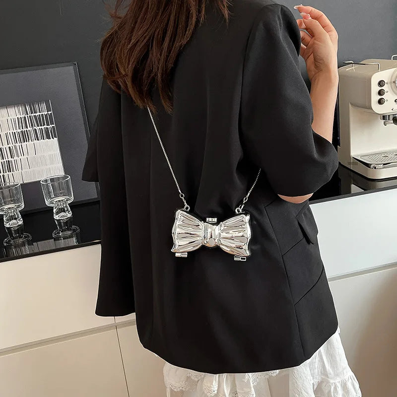 A woman holds a black blazer featuring an acrylic bow clasp mini handbag with a silver chain strap.