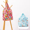 A pink floral reusable shopping bag hanging on a wooden rack next to a light blue patterned bag.