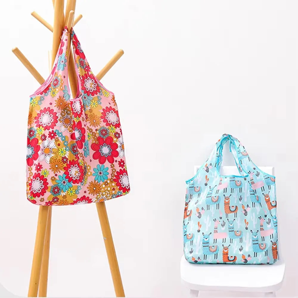 A pink floral reusable shopping bag hanging on a wooden rack next to a light blue patterned bag.