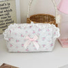 A white cosmetic storage pouch with pink floral print and a pink bow, resting on a white surface.