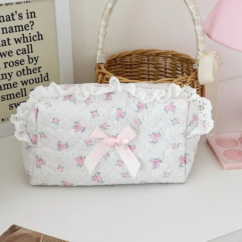A white cosmetic storage pouch with pink floral print and a pink bow, resting on a white surface.