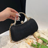 A hand holds a black glitter crossbody evening clutch bag with gold chain detailing and white tulips.