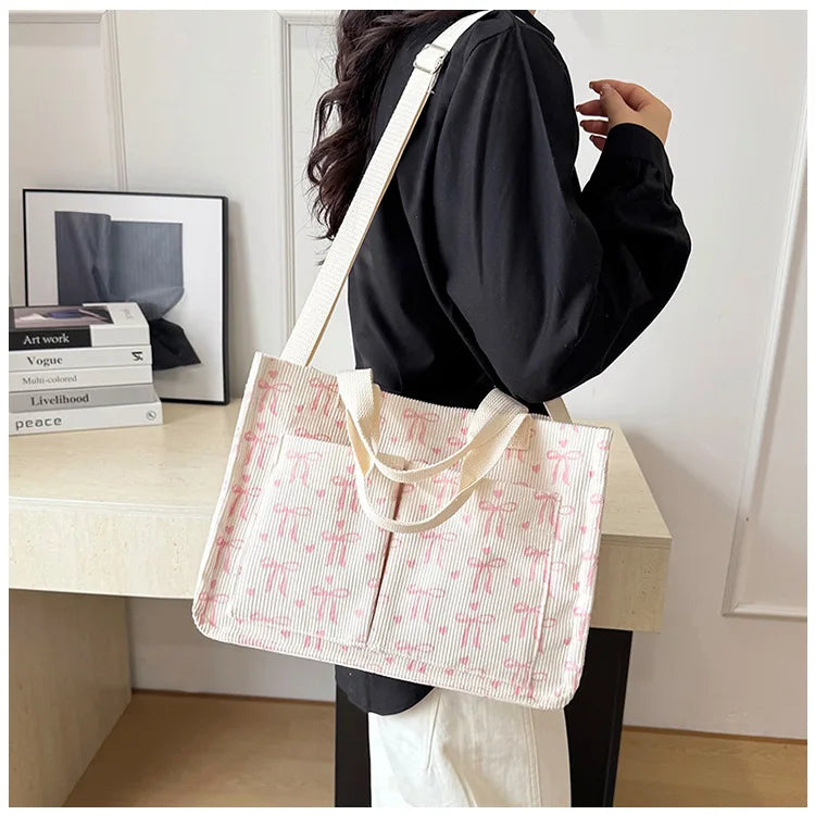 A light pink canvas tote bag with a repeating strawberry pattern is displayed on a wooden table.