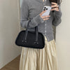 A woman wearing a gray sweater and light skirt holds a black crocodile textured mini crossbody bag and a smartphone.