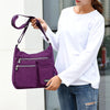 Eine Frau hält eine lila, wasserdichte Nylon-Crossbody-Tasche vor einem unscharfen Hintergrund.