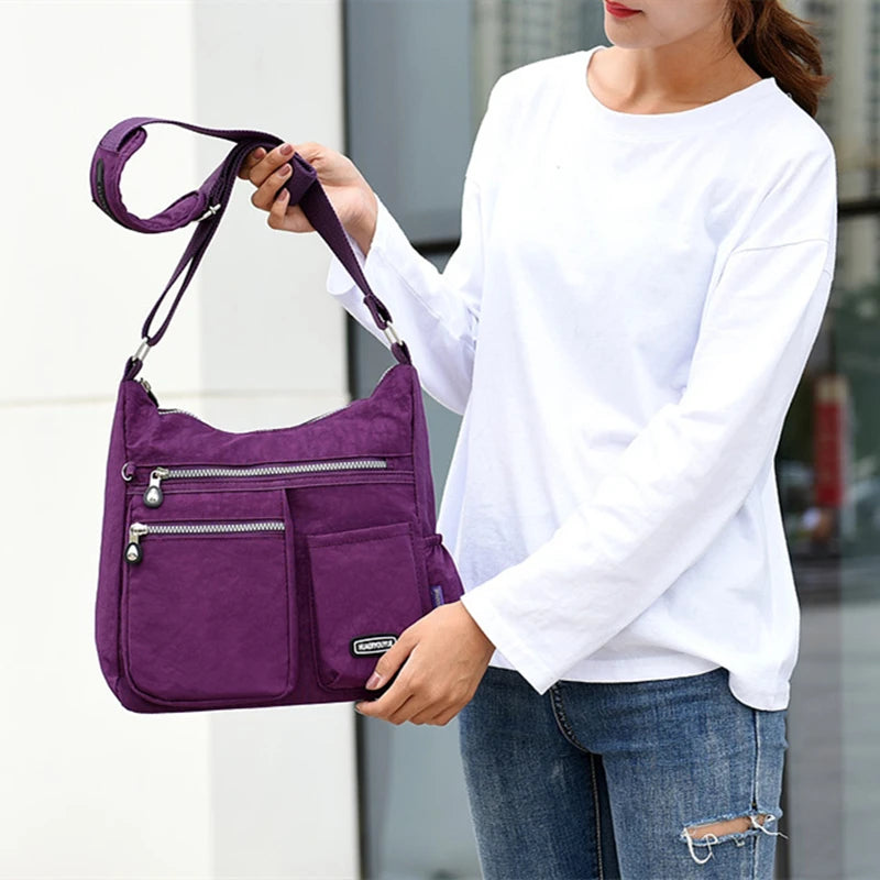 Eine Frau hält eine lila, wasserdichte Nylon-Crossbody-Tasche vor einem unscharfen Hintergrund.