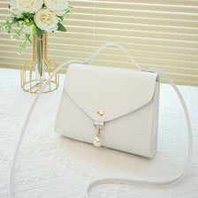 A light beige beaded square crossbody bag with a white adjustable strap resting on a white surface.