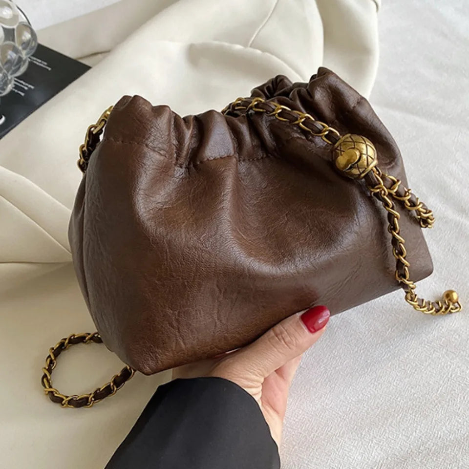 A brown PU leather chain shoulder bag with a gold chain strap is held in a hand against a white background.