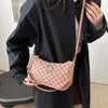 Una mujer sostiene un bolso cruz rosa y dorado con forma de M contra un abrigo negro.