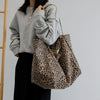 A woman models a leopard print canvas crossbody tote bag with a gray sweatshirt and black skirt.