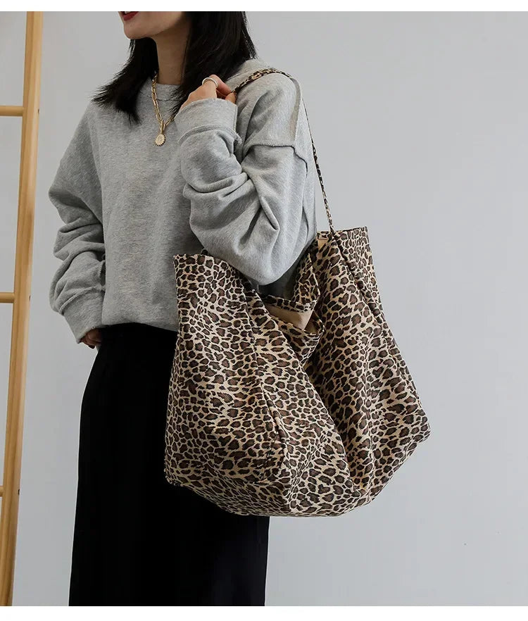 A woman models a leopard print canvas crossbody tote bag with a gray sweatshirt and black skirt.