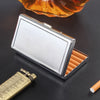 A silver metal cigarette holder with an open tray is shown next to a glass of amber liquid and a measuring tool.