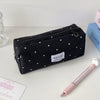 Eine schwarze Polka-Dot-Pencilcase neben einem rosa Bleistift und einem blauen Buch